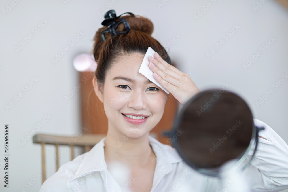 Naklejka premium Portrait of a Beauty young woman brunette cosmetics looking in the mirror using tissue with toner for cleaning make up with fresh healthy facial skin,feeling so fresh and happiness,Beauty and Cosmetic