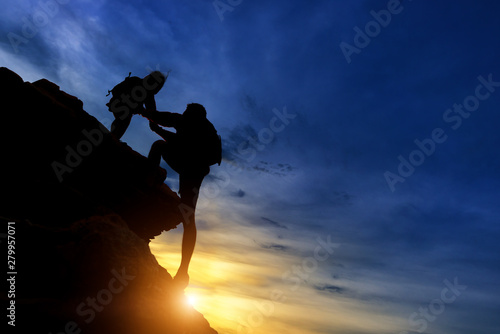 Silhouette of the climbing team helping each other while climbing up in a sunset. The concept of aid.