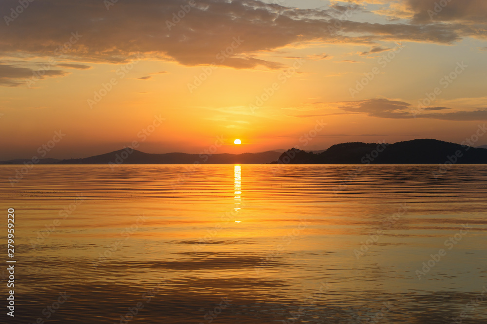 Beautiful cloudy sunset and sea landscape. Gold colored sky and sea, hills silhouette in the evening.