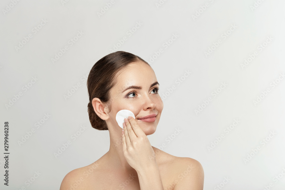 Beauty portrait of a cheerful young topless woman removing face make-up with a cotton pad