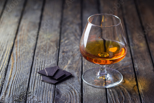 Glasse of brandy or cognac and chocolate on dark background.