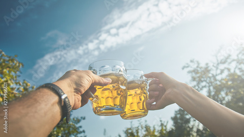 Pair holding beer glasses in the air from personal point of view - POV.