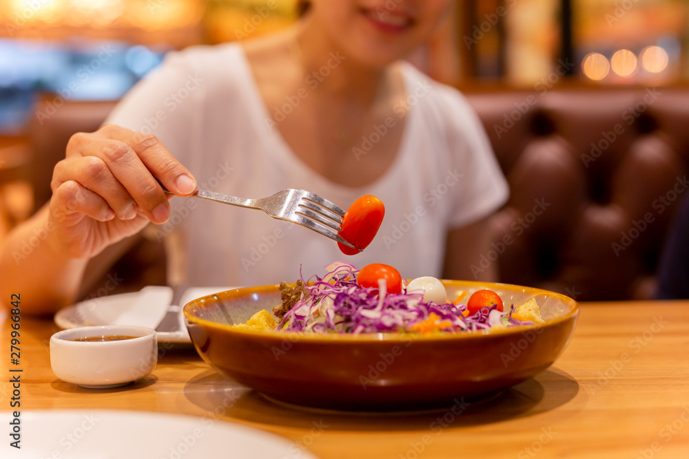 Woman eating salad with hand holding fork and tomato in her hand. Woman eating salad with hand holding fork and tomato in her hand.