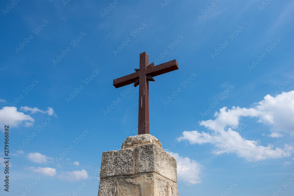 A Christian cross under a blue sky with clouds