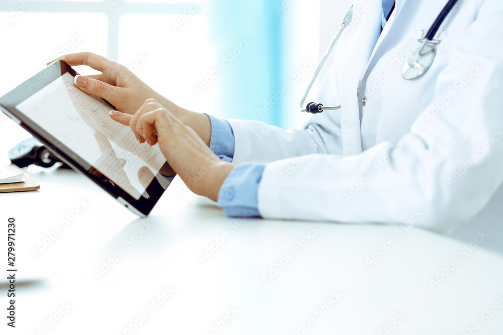 Doctor working table. Woman physician using tablet computer while sitting in hospital office close-up. Healthcare, insurance and medicine concept Doctor working table. Woman physician using tablet computer while sitting in hospital office close-up. Healthcare, insurance and medicine concept