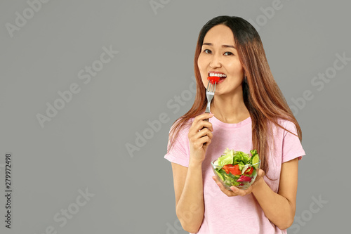 Asian woman with vegetable salad on grey background