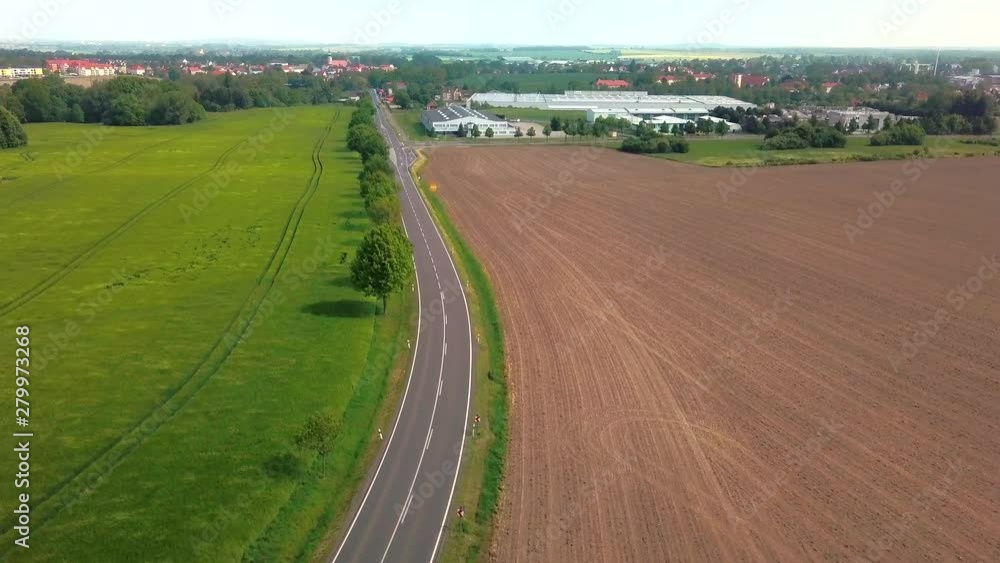 Aerial view of crop field blowing in the wind with road winding through it and small city in the background Aerial view of crop field blowing in the wind with road winding through it and small city in the background