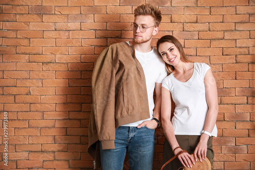 Couple in stylish t-shirts against brick wall