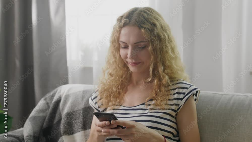 Young cute girl typing a message on the smartphone in the living room Young cute girl typing a message on the smartphone in the living room