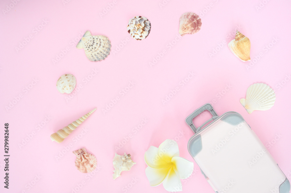 Frame of stylish summer suitcase and white flower, shell on pink background, top view with place for text. Concept for sea travel