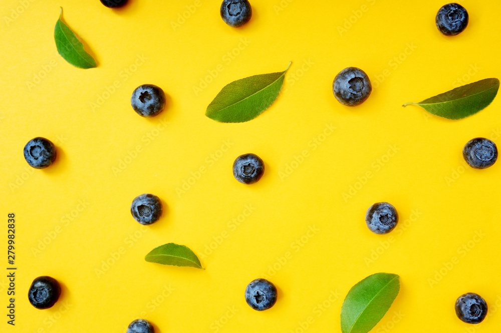 Fototapeta premium Summer blueberries with leaf on yellow background. Berries design backdrop. Close up top view or flat lay
