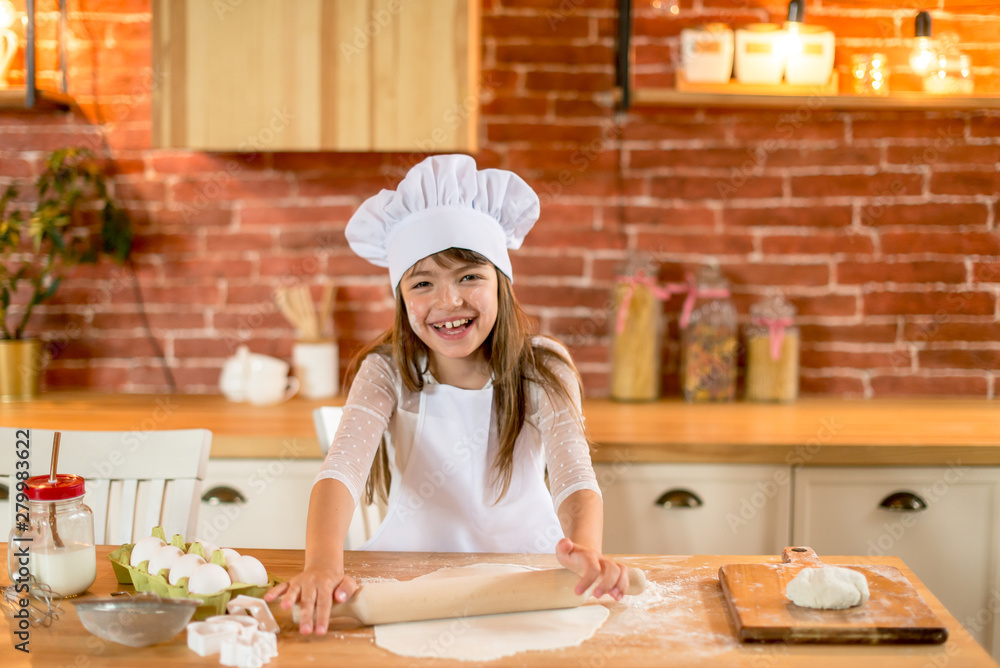 Happy girl 7 years old in chef clothes is standing at the table. A girl in chef clothes sifts flour through a sieve. Homemade food concept. Happy girl 7 years old in chef clothes is standing at the table. A girl in chef clothes sifts flour through a sieve. Homemade food concept.