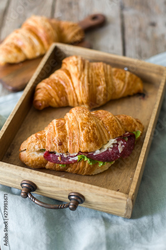 Croissant sandwich on the wooden table with salami, cheese and fresh salad food photography