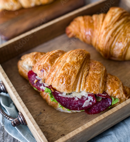 Croissant sandwich on the wooden table with salami, cheese and fresh salad food photography