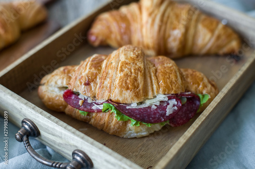 Croissant sandwich on the wooden table with salami, cheese and fresh salad food photography