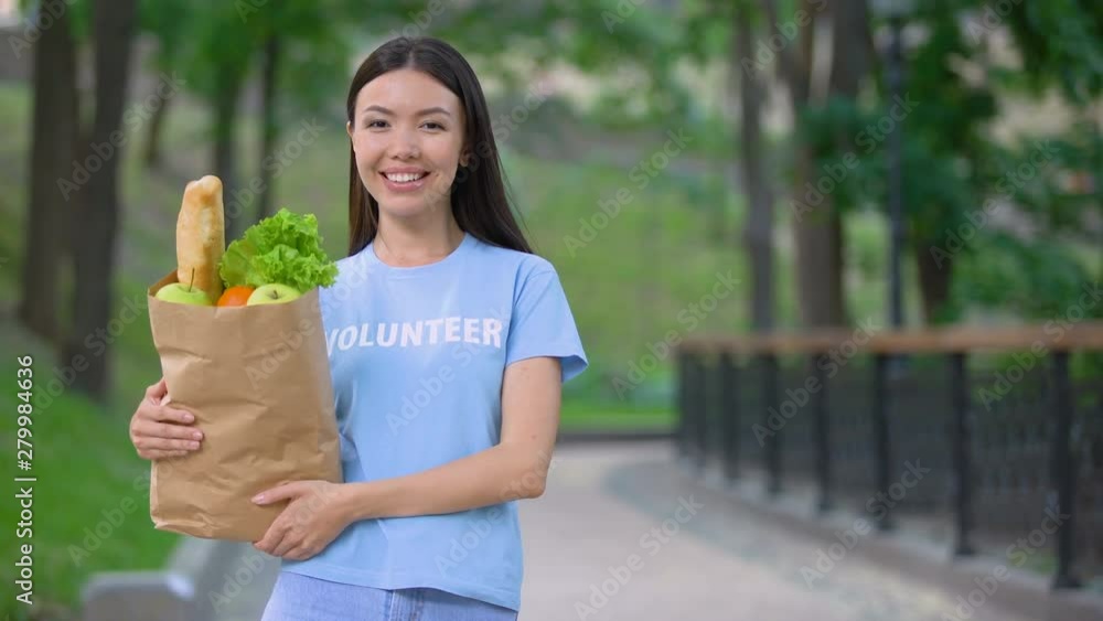 Cheerful female volunteer holding grocery bag outdoors smiling camera, donation Cheerful female volunteer holding grocery bag outdoors smiling camera, donation