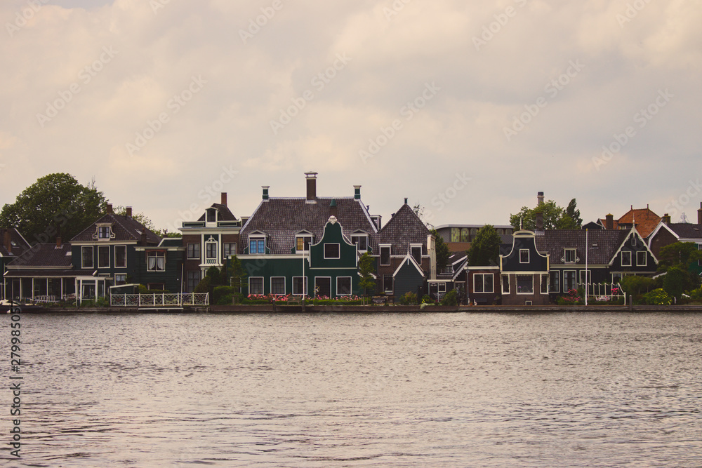 Obraz premium Typical dutch buildings on the river side faded. Holland architecture filtered. Country houses in Zaanse Schans, Netherlands. Rural buildings on the lake. Summer travel concept. Summer countryside.