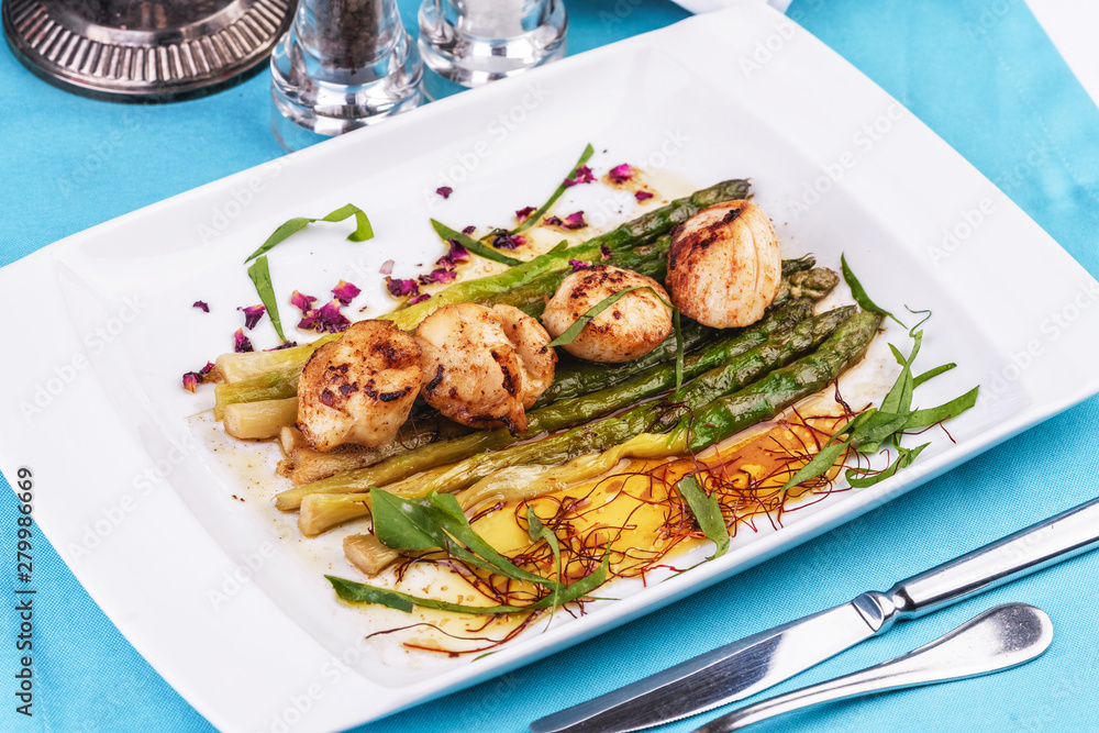  European recipe, Mediterranean dish. Caramelized asparagus with onion chips, rose petals, arugula and pieces of fried fish