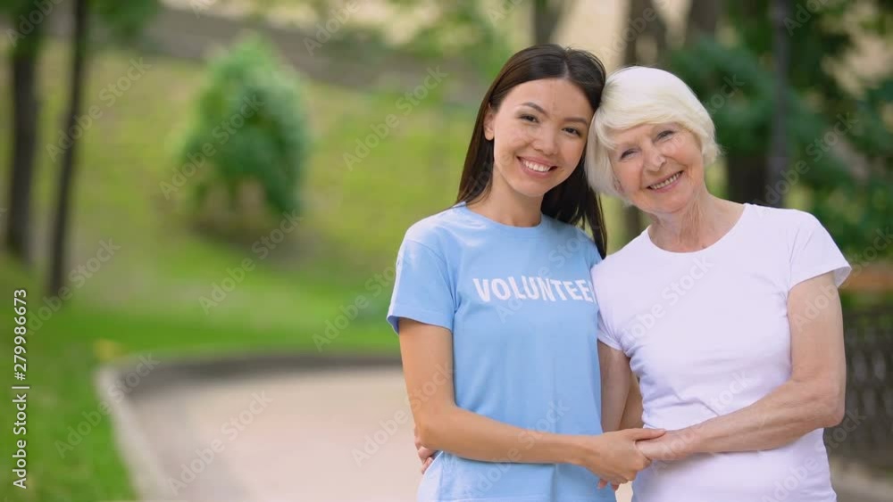 Female volunteer and happy elderly lady holding hands smiling camera, support Female volunteer and happy elderly lady holding hands smiling camera, support