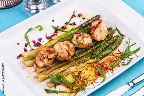  European recipe, Mediterranean dish. Caramelized asparagus with onion chips, rose petals, arugula and pieces of fried fish