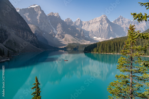 single red canoe in middle of Moraine Lake with blue skies and reflected mountains Alberta Canada