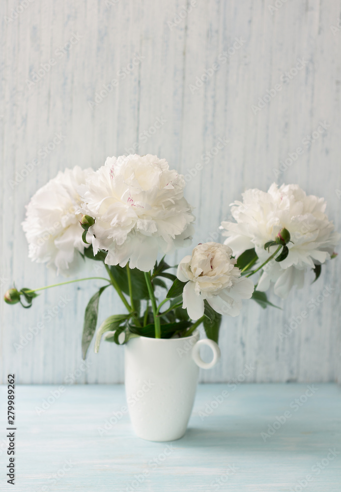 Garden white peonies with lilac border in a white porcelain vase on a light blue wooden background, close up Garden white peonies with lilac border in a white porcelain vase on a light blue wooden background, close up