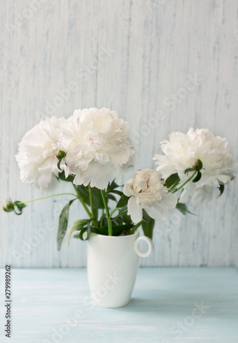 Garden white peonies with lilac border in a white porcelain vase  on a light blue wooden background, close up