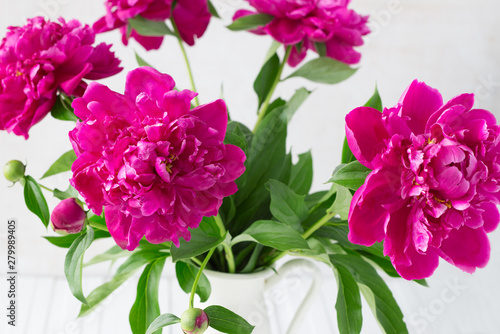 Purple garden peonies in a white enamel jug on a white wooden background  rustic style  close up
