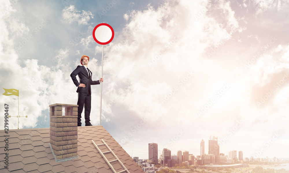 Caucasian businessman on brick house roof showing stop road sign Caucasian businessman on brick house roof showing stop road sign