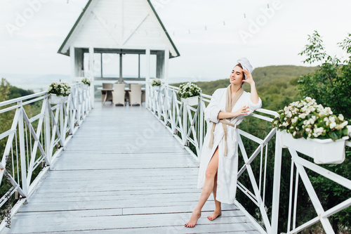 Morning concept. Portrait of pretty, young woman resting in luxury resort in mountains, stay on villa terrace and posing, wearing at white robe.