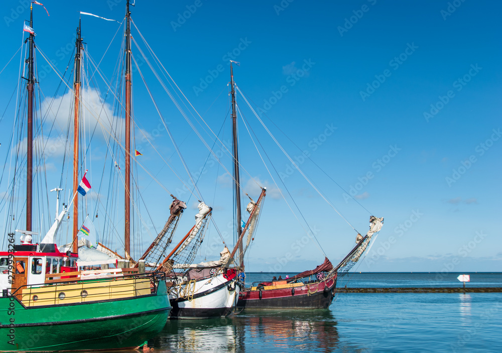 Three sailboats in a row in blue water with blue sky above it. Terschelling, The Netherlands, Europe.