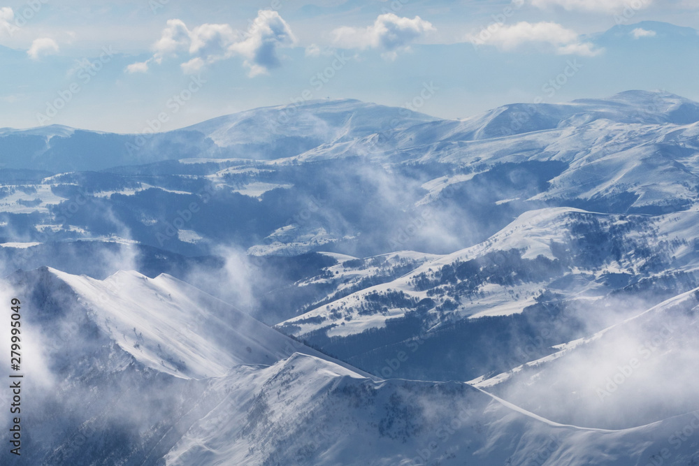 Fototapeta premium Snowy sunlight mountains in fog and multicolor cloudy sky
