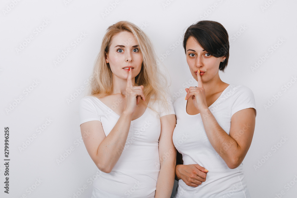 Two attractive women showing a silence gesture and looking at the camera