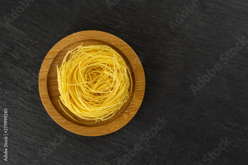 One whole raw pasta angel hair on bamboo plate flatlay on grey stone photo
