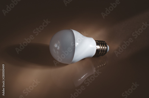 LED lamp on a glass surface with reflection and shadow. Snapshot on a dark background. Frame top angled with negative empty space close-up