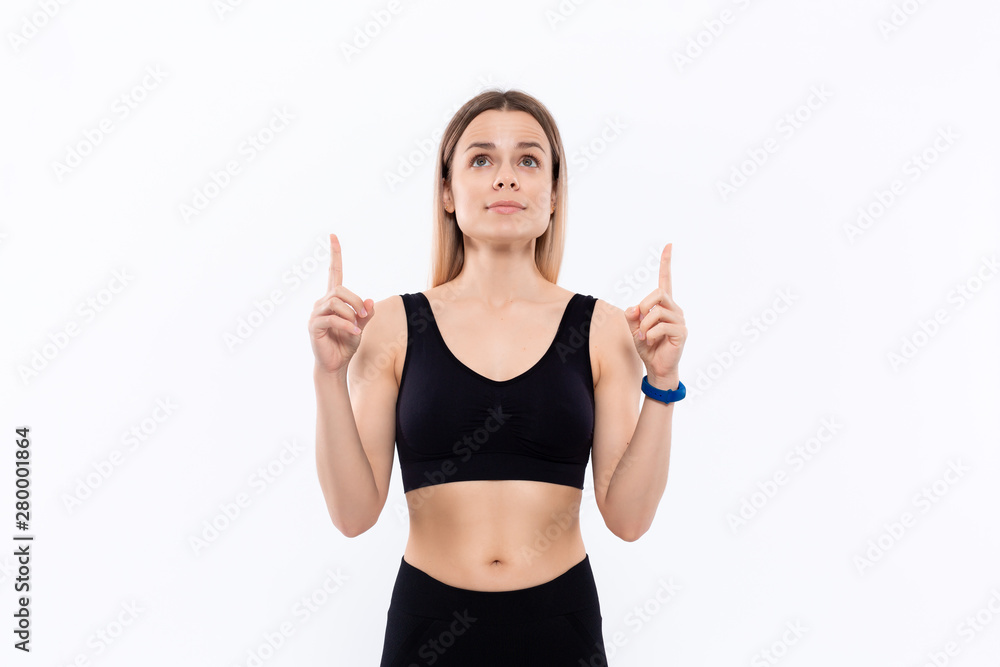 Young sporty blond woman in a black sportswear with smart watches for pulse measuring pointing with fingers up. Young sporty blond woman in a black sportswear with smart watches for pulse measuring pointing with fingers up.