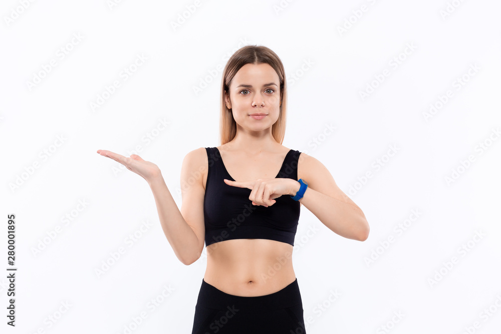 Young sporty blond woman in a black sportswear with smart watches for pulse measuring pointing with one hand at the pulm of a hand Young sporty blond woman in a black sportswear with smart watches for pulse measuring pointing with one hand at the pulm of a hand