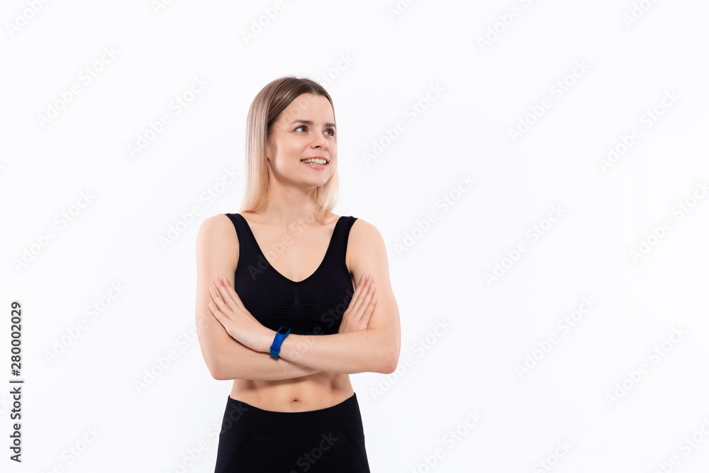 Young sporty blond woman in a black sportswear with smart watches for pulse measuring keeping hands crossed standing over white background. Young sporty blond woman in a black sportswear with smart watches for pulse measuring keeping hands crossed standing over white background.