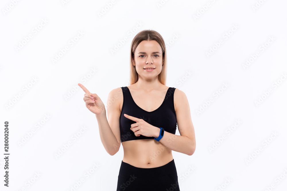 Young sporty blond woman in a black sportswear with smart watches for pulse measuring pointing with fingers to the left. Young sporty blond woman in a black sportswear with smart watches for pulse measuring pointing with fingers to the left.