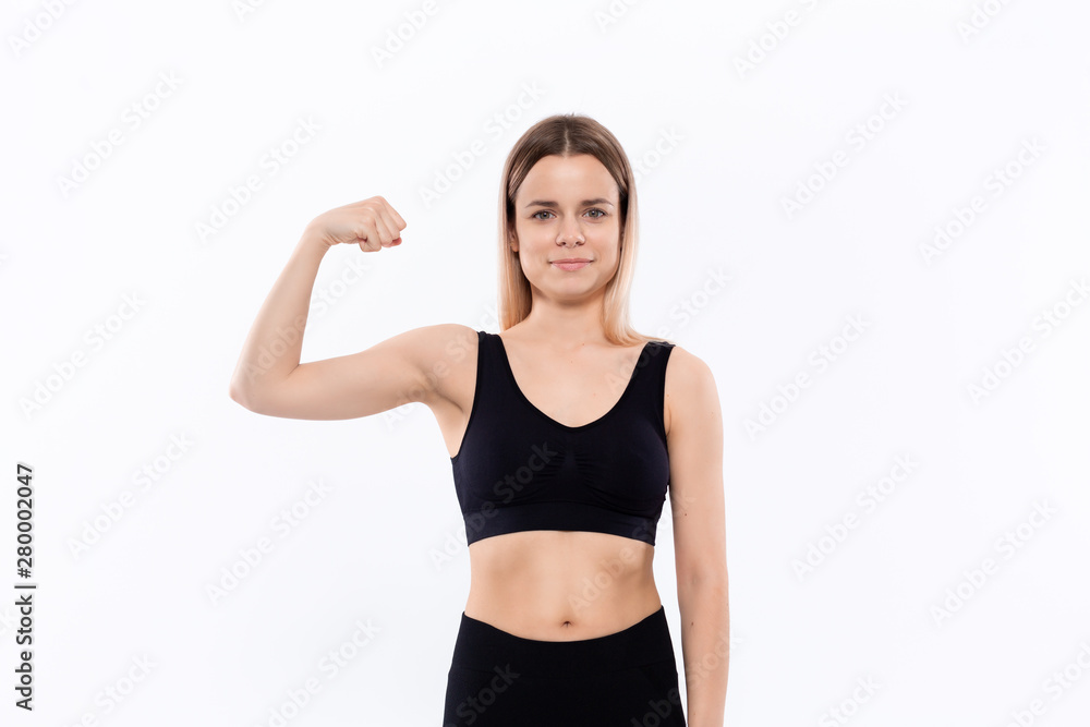 Young sporty blond woman in a black sportswear showing bicep standing over white background Young sporty blond woman in a black sportswear showing bicep standing over white background
