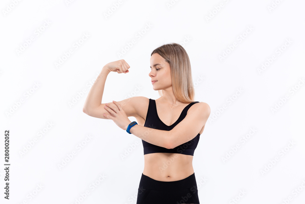 Young sporty blond woman in a black sportswear  showing bicep standing over white background