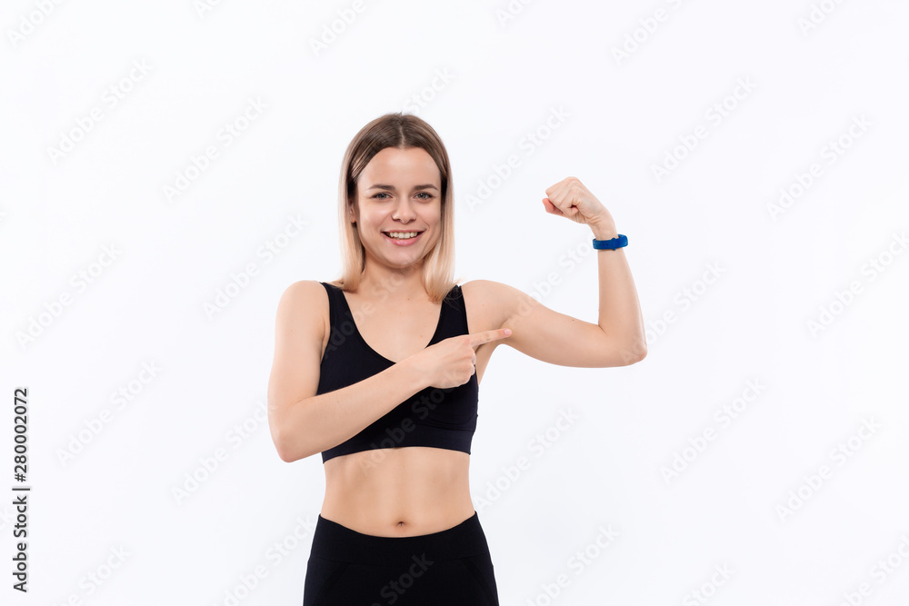Happy young sporty blond woman in a black sportswear showing bicep standing over white background Happy young sporty blond woman in a black sportswear showing bicep standing over white background