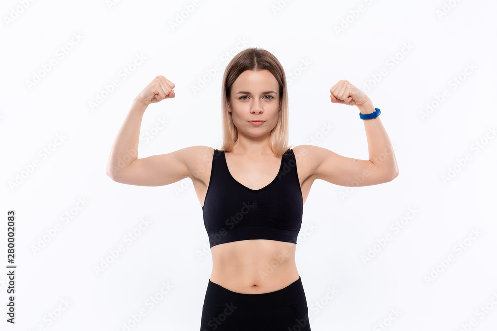 Young sporty blond woman in a black sportswear showing bicep standing over white background Young sporty blond woman in a black sportswear showing bicep standing over white background