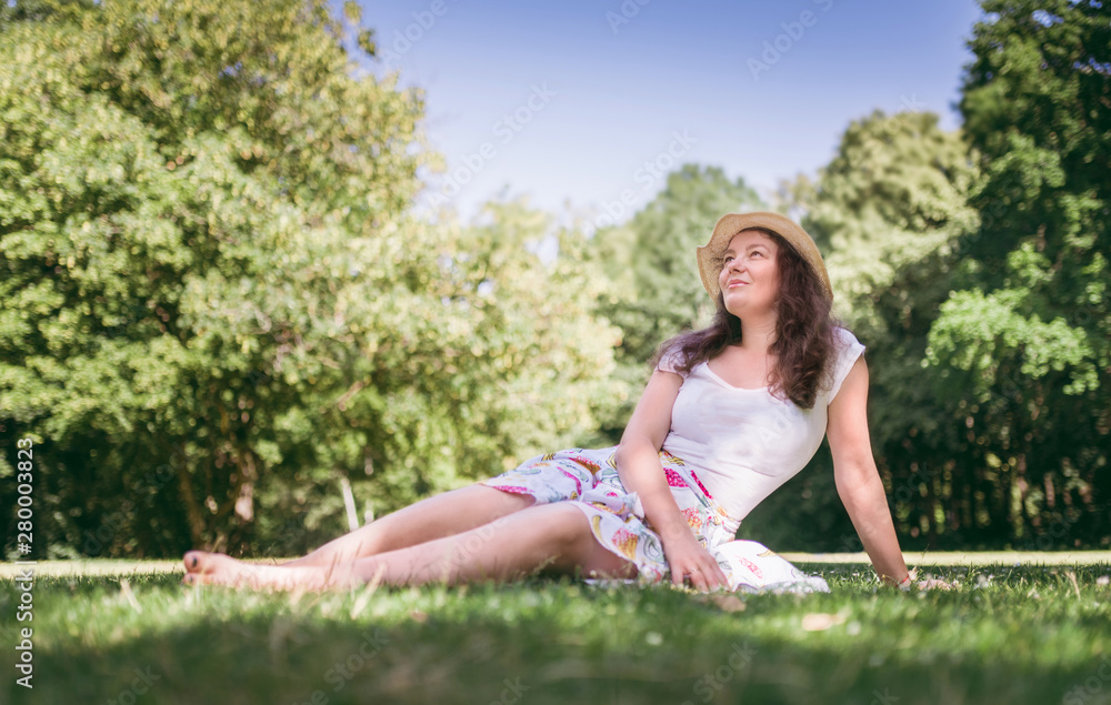 Summer portrait of young  woman sitting on the grass, in sunny day. Beautiful, romantic woman looking to the sky.