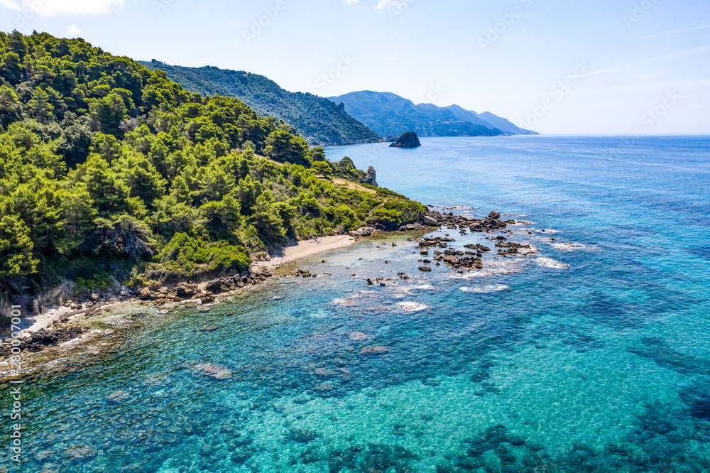 Aerial view of green seashore and turquoise sea water. Island with green trees in the ocean seen form above.