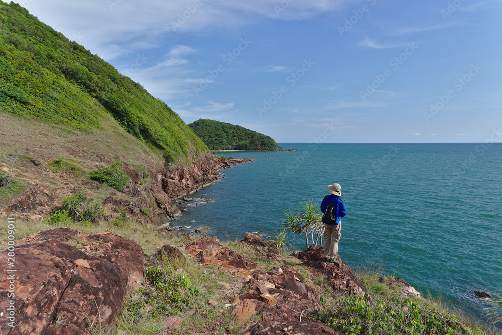 Female explorer standing on the rock on the edge of the cliff staring at the island next to the cape.