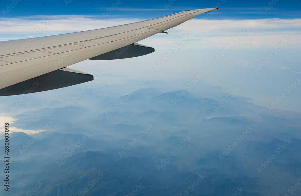 Wing of plane over mountain. Airplane flying on blue sky and white clouds. Scenic view from airplane window. Commercial airline flight. Plane wing. Flight mechanics concept. International flight. Wing of plane over mountain. Airplane flying on blue sky and white clouds. Scenic view from airplane window. Commercial airline flight. Plane wing. Flight mechanics concept. International flight.