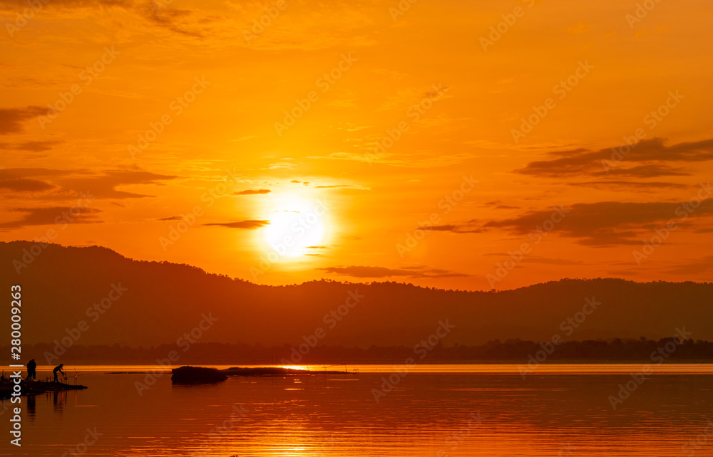 Beautiful sunrise sky above the mountain at reservoir. People are fishing with a fishing rod on the river. Landscape of reservoir and mountain with orange sunrise sky. Silhouette life in the morning.
