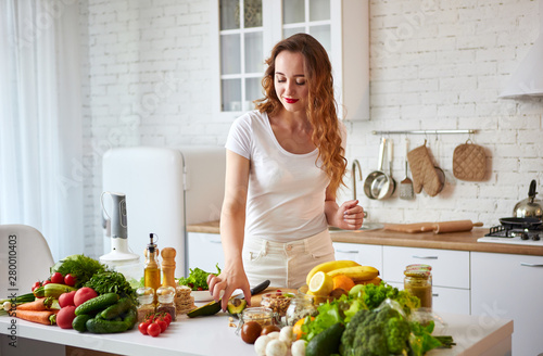 Young happy woman preparing tasty salad in the beautiful kitchen with green fresh ingredients indoors. Healthy food and Dieting concept. Loosing Weight