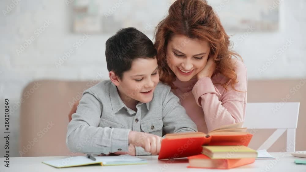 smiling mother helping son with homework while he reading book at desk smiling mother helping son with homework while he reading book at desk